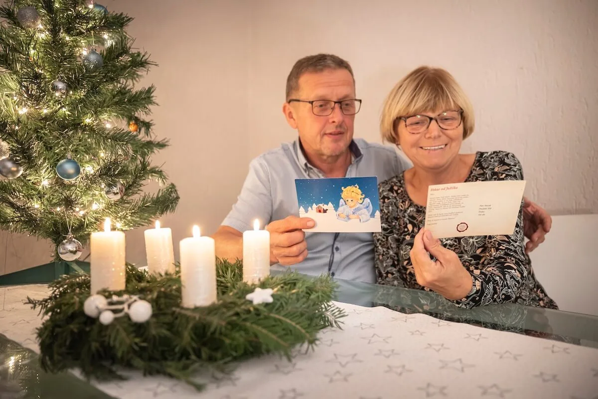 Manželia pri adventnom venci sa s úsmevom pozerajú na pohľadnicu od Ježiška